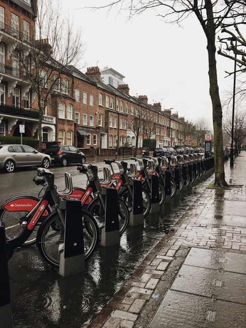A large multi-storey brick building with arched windows and decorative brickwork, situated above a street-level parking area for bicycles and vehicles near Tufnell Park tube station. The scene include